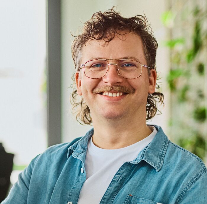 Employee Tobias Dühr sitting in the office on a desk, smiling
