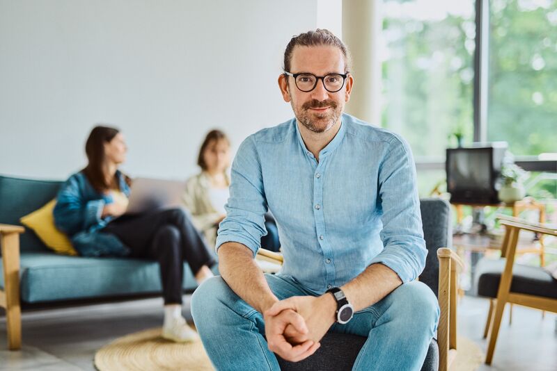 Employee Martin Schittig sitting in the office on an armchair, smiling