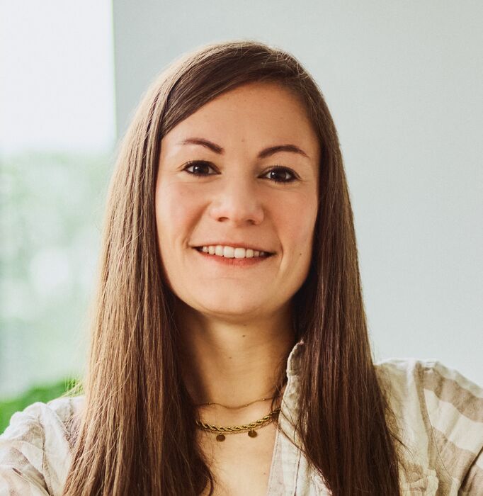 Employee Theresa Seubert sitting in the office on a desk with a laptop, smiling