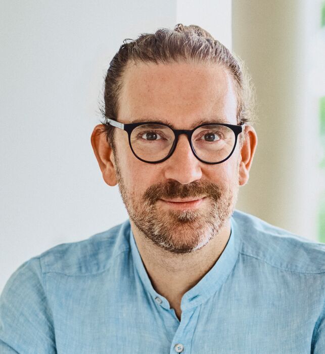 Employee Martin Schittig sitting in the office on an armchair, smiling