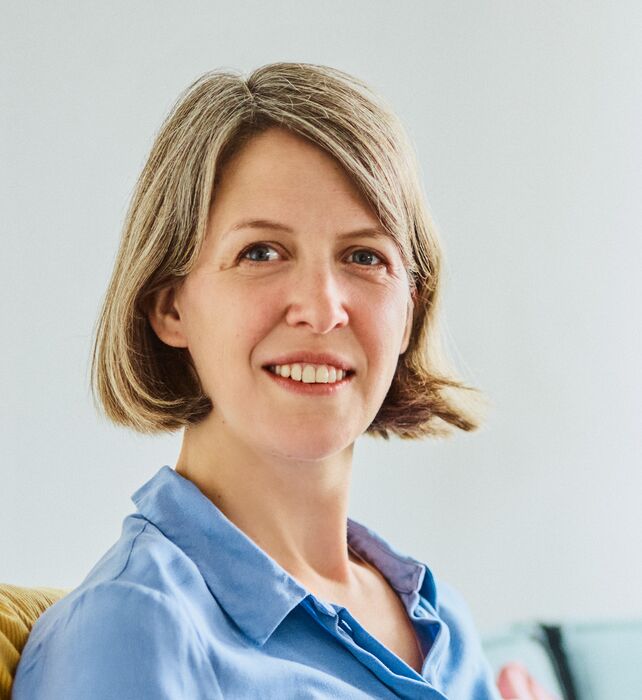Employee Jutta Kriegsmann sitting in the office on a couch with a laptop, smiling